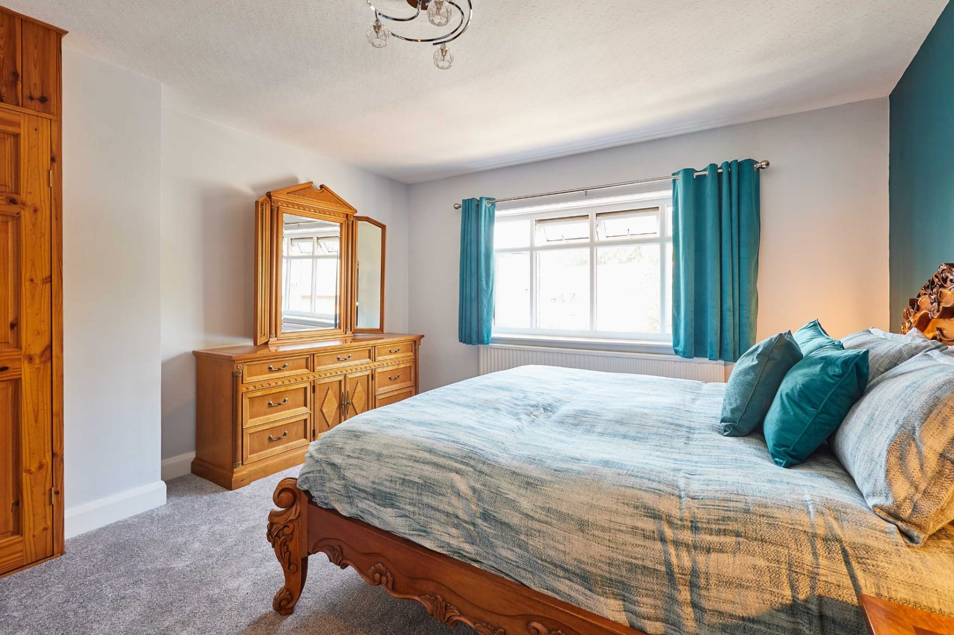 Double bedroom with teal curtains and carved wooden bed