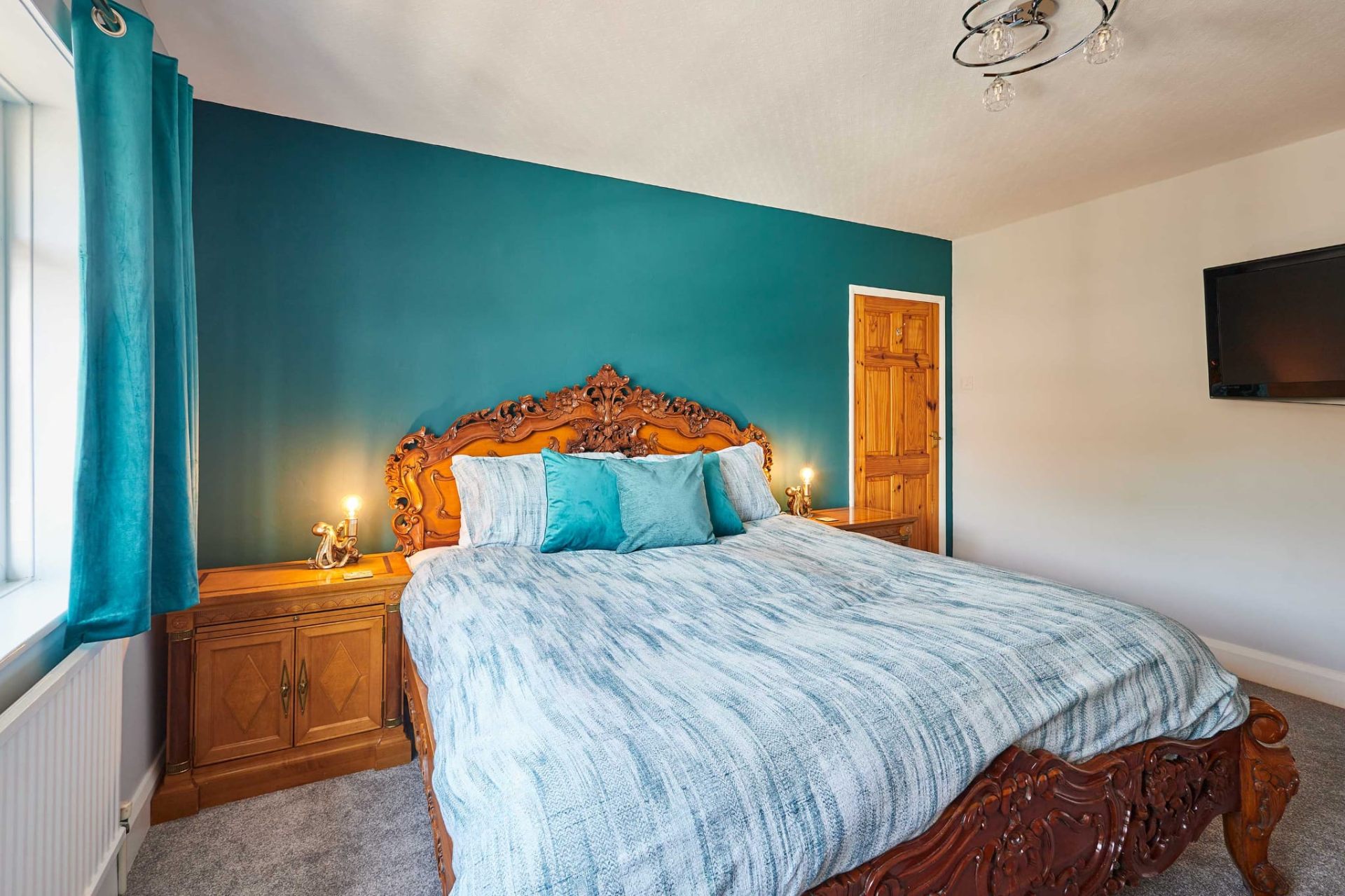 Master bedroom with teal feature wall and ornate carved kingsize bed
